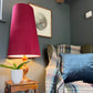 Chair with plaid blanket and blue pillow next to a lamp with a red shade on a wooden side table.