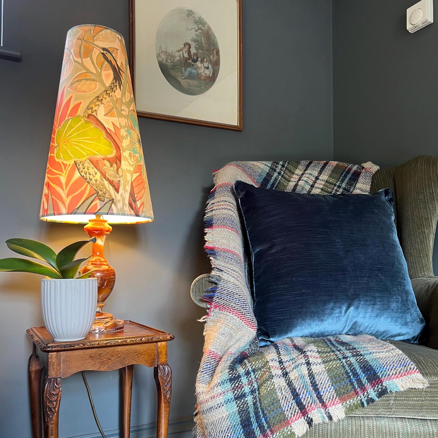 Living room corner with a lamp, plant, and sofa with plaid blanket and blue pillow.