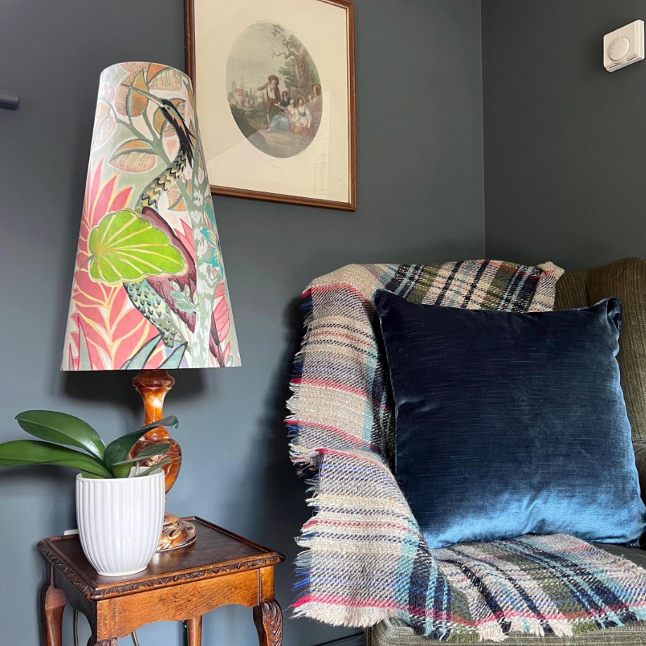 Decorative lamp with colorful shade on a side table next to a sofa with cushions and a blanket.